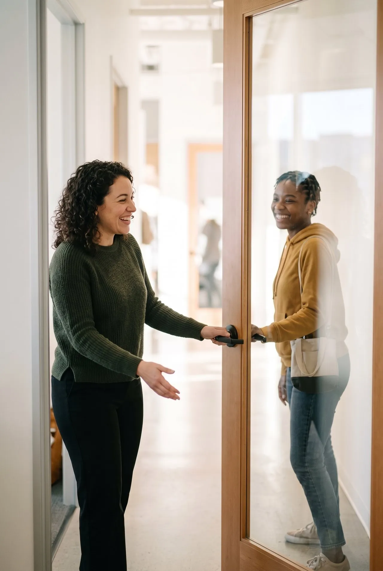 A nonprofit staffer welcomes a first-time visitor at a bright office doorway, both mid-greeting